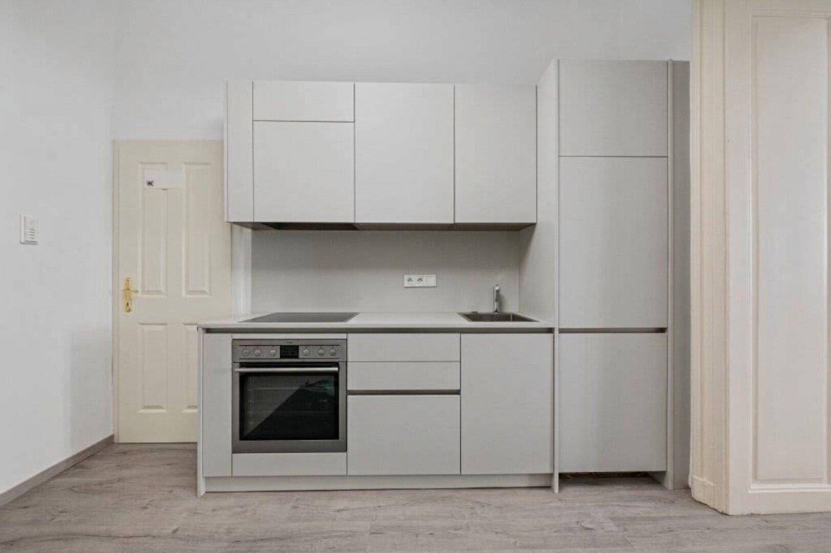 Moderne Küchenzeile mit grauen Schränken, integriertem Backofen und Kochfeld, ideal für kleine Räume.