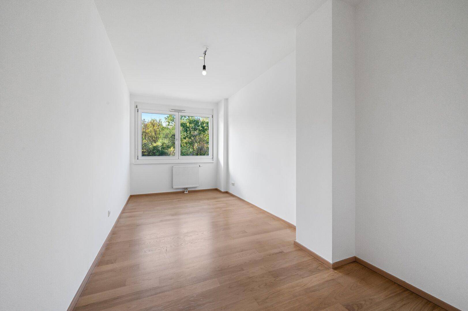 Geräumiges Zimmer mit Parkettboden und Fenster, vielseitig nutzbar als Schlaf- oder Arbeitszimmer.