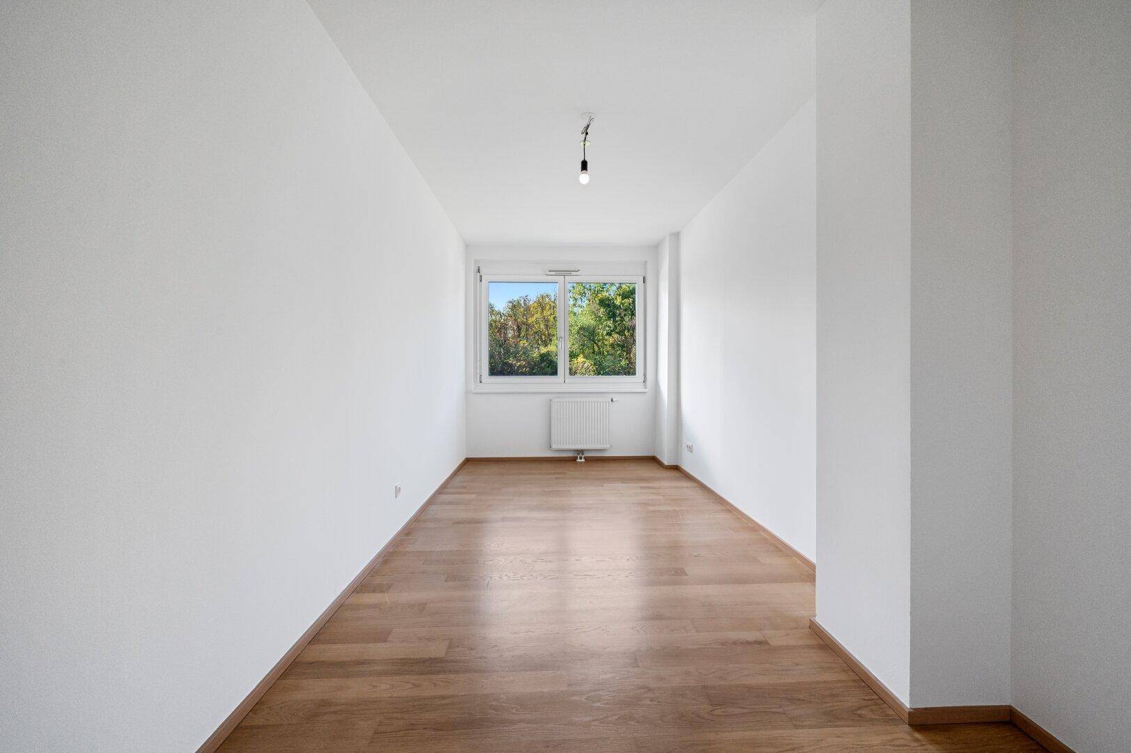 Helles Zimmer mit Parkettboden und Fenster, bietet viel Potenzial für individuelle Einrichtung.
