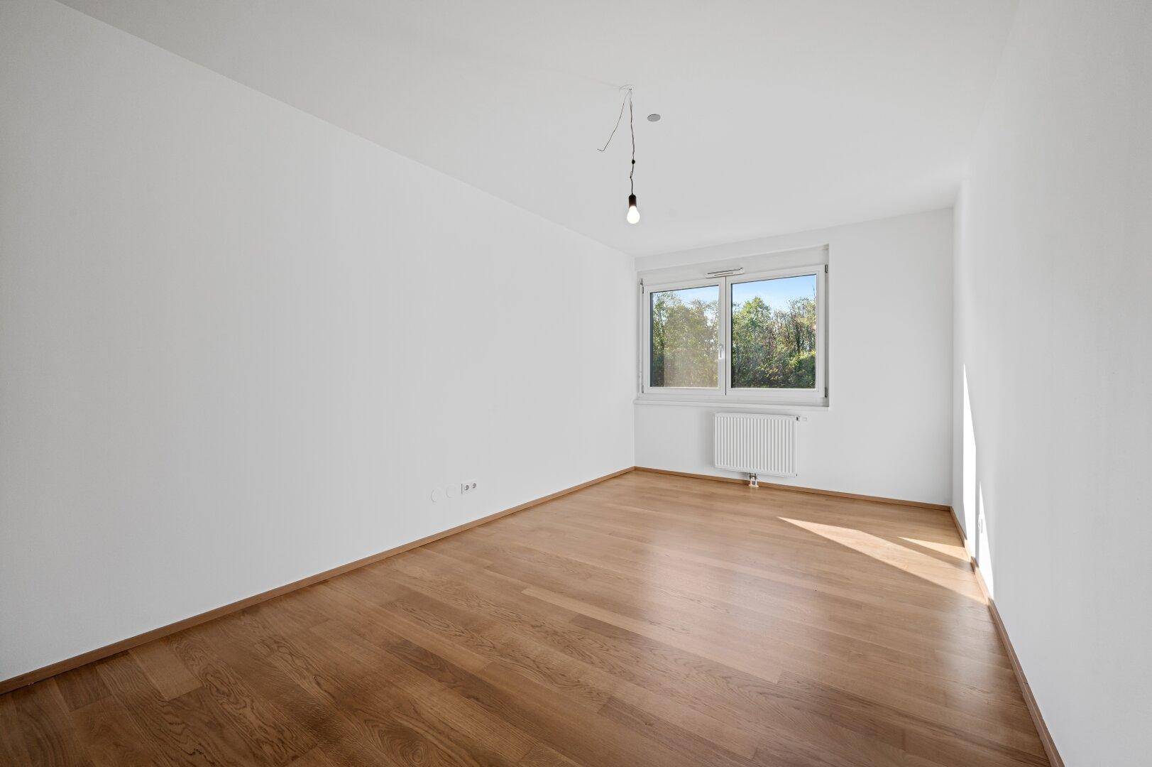 Helles Schlafzimmer mit Parkettboden und Fenster, bereit zur individuellen Gestaltung.