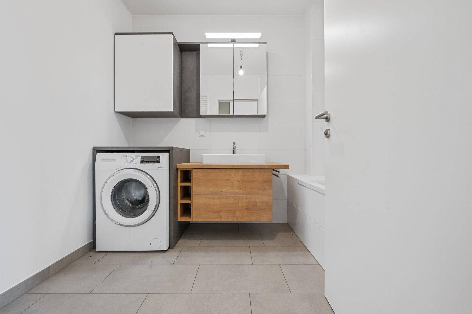 Modernes Badezimmer mit Waschmaschine, Holzwaschtisch und Spiegelschrank.