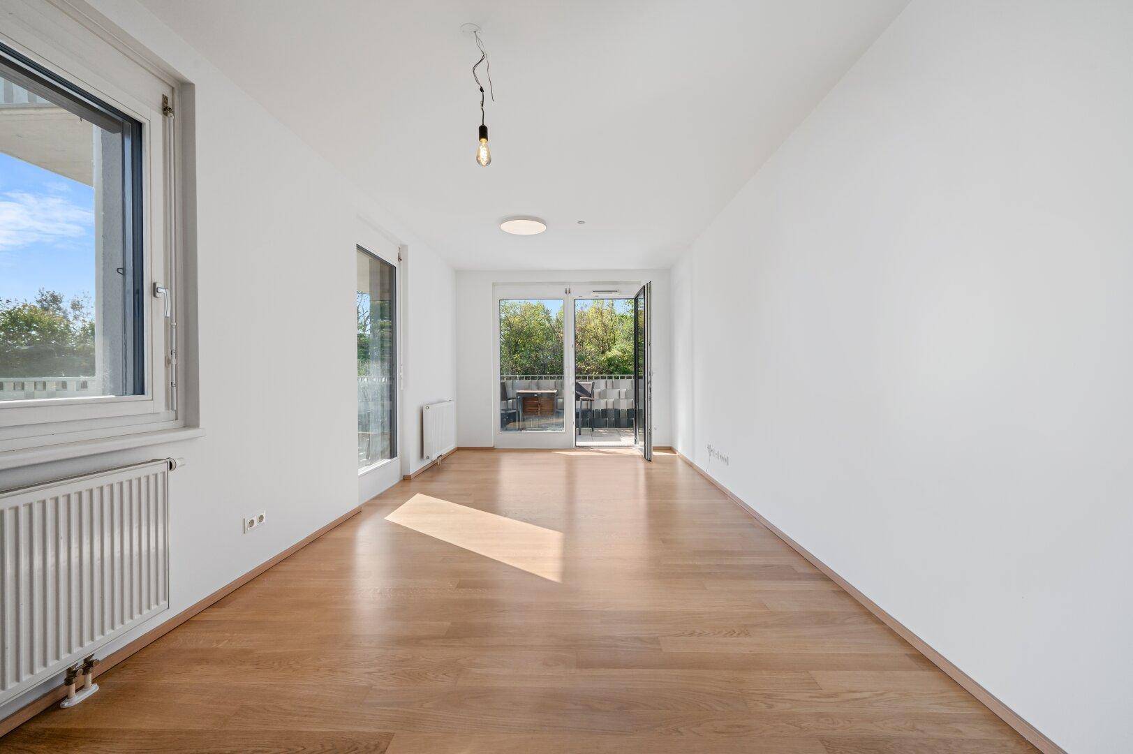 Lichtdurchflutetes Wohnzimmer mit Holzboden und Zugang zu einem kleinen Balkon.