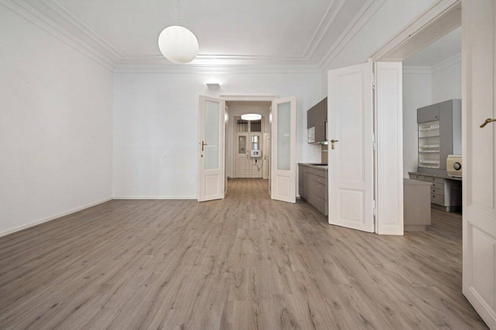 Geräumiger, leerer Raum mit Laminatboden und offenen Türen zu Küche und Flur.