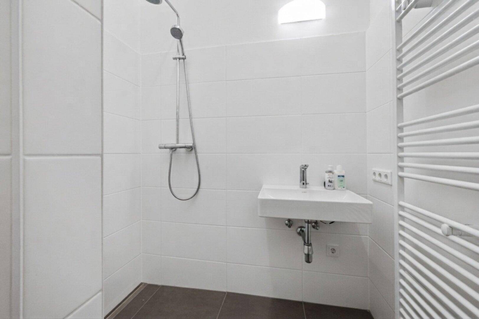 Modernes Badezimmer mit Dusche, kleinem Waschbecken und beheiztem Handtuchhalter.