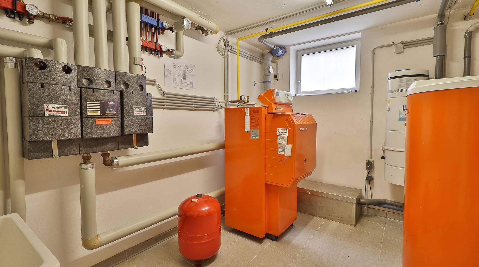 Technikraum mit Heizungsanlage, Warmwasserspeicher und sichtbaren Rohrleitungen.