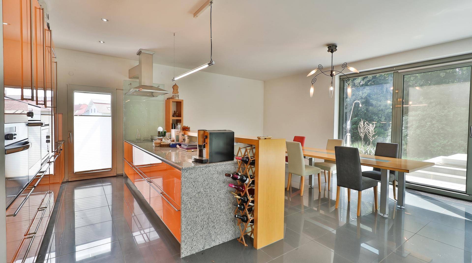 Moderne offene Küche mit orangefarbenen Schränken, Kücheninsel und Essbereich mit Zugang zur Terrasse.