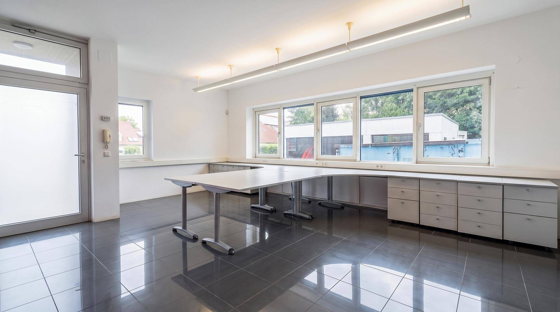 Großes, helles Büro oder Atelier mit langen Arbeitsflächen und vielen Fenstern.