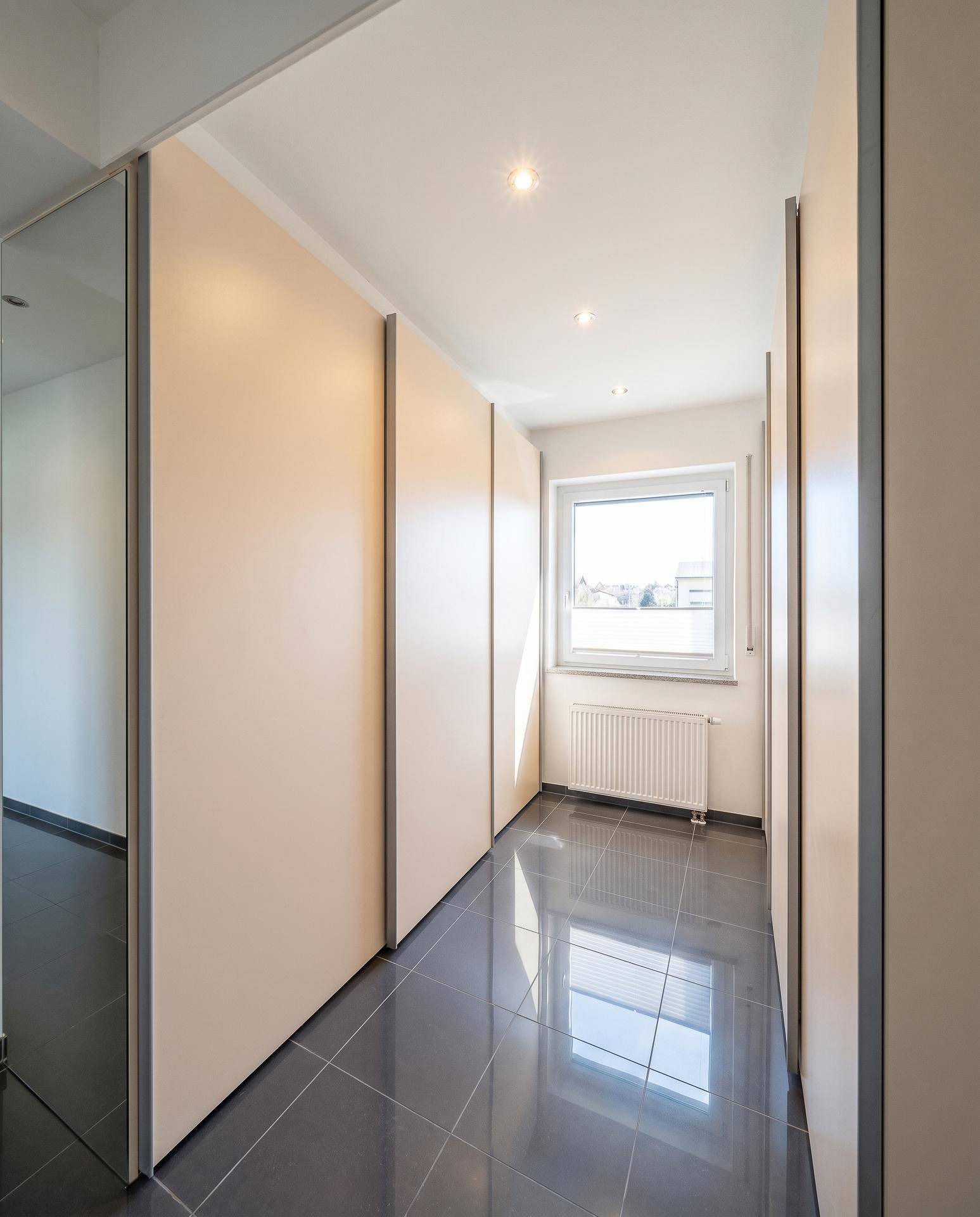 Heller Flur mit Einbauschränken und einem Fenster, das Tageslicht hereinlässt.