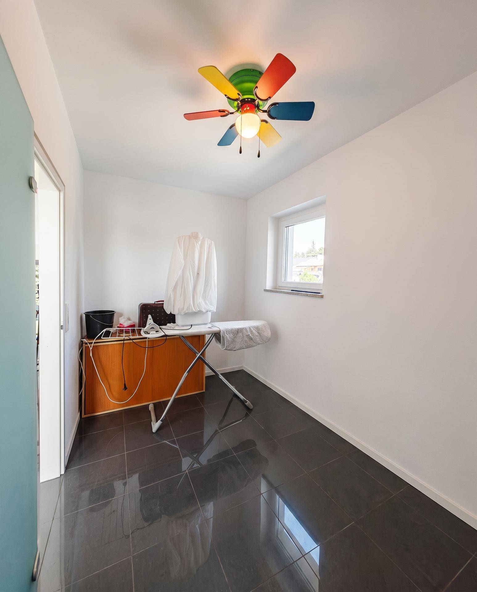 Praktischer Hauswirtschaftsraum mit Bügelbrett, Schrank und farbenfrohem Deckenventilator.