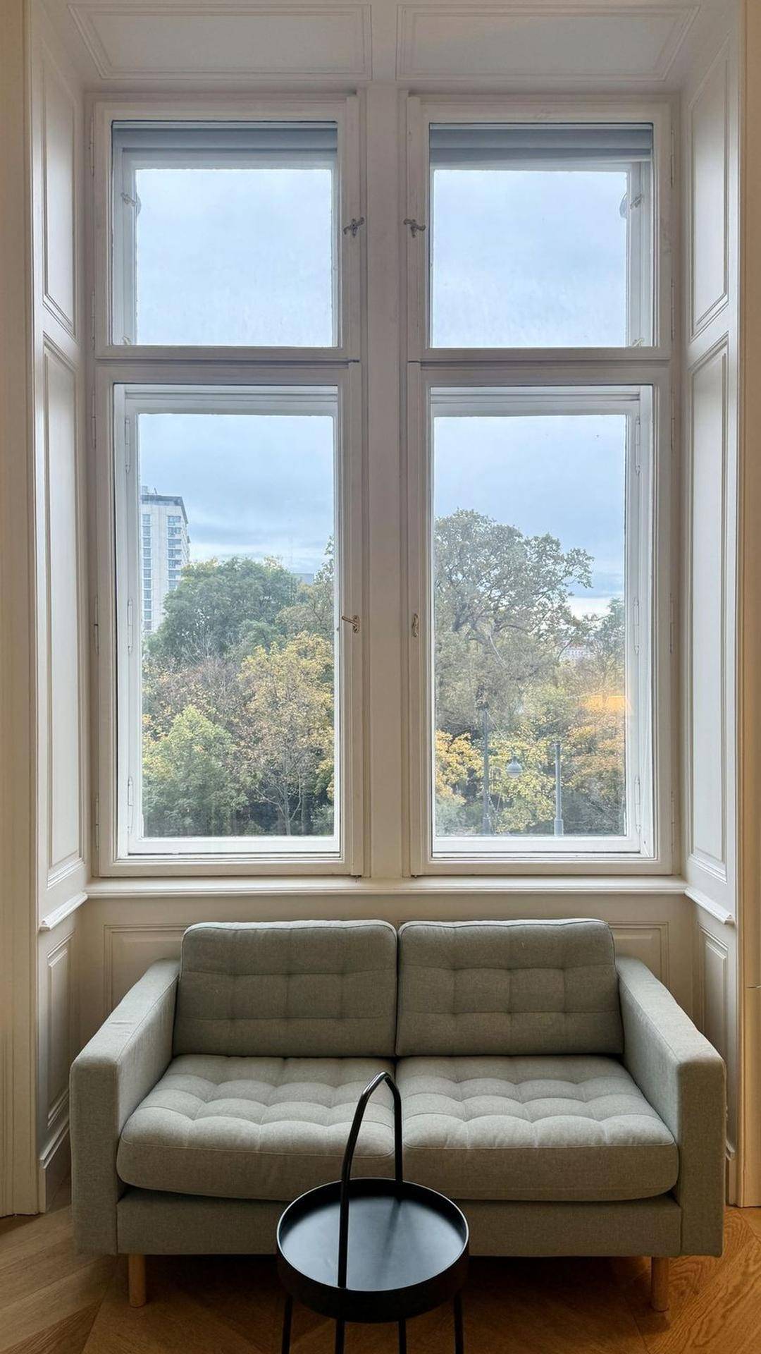 Helles Wohnzimmer mit bequemer Couch und großen Fenstern mit Blick ins Grüne.