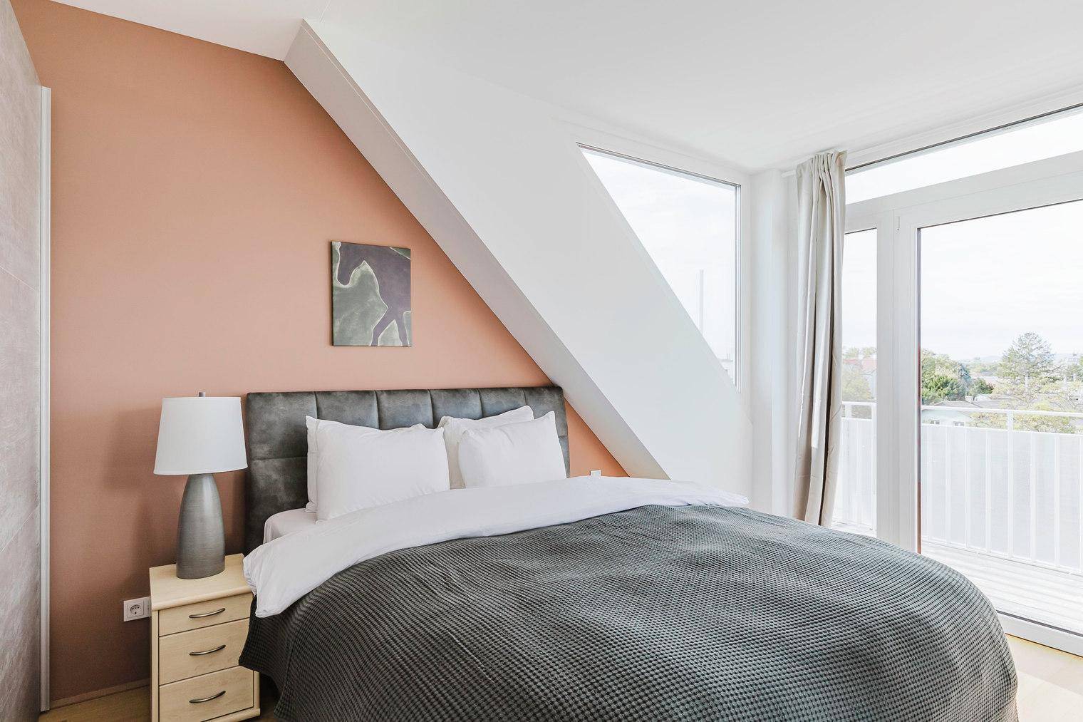 Helles Schlafzimmer mit Dachschräge, rosafarbener Akzentwand und Zugang zur Terrasse.
