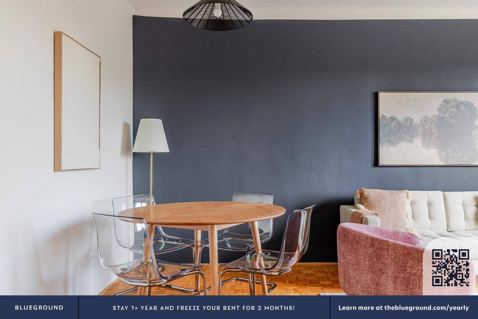 Essbereich mit rundem Holztisch und modernen transparenten Stühlen vor einer dunkelgrauen Wand.