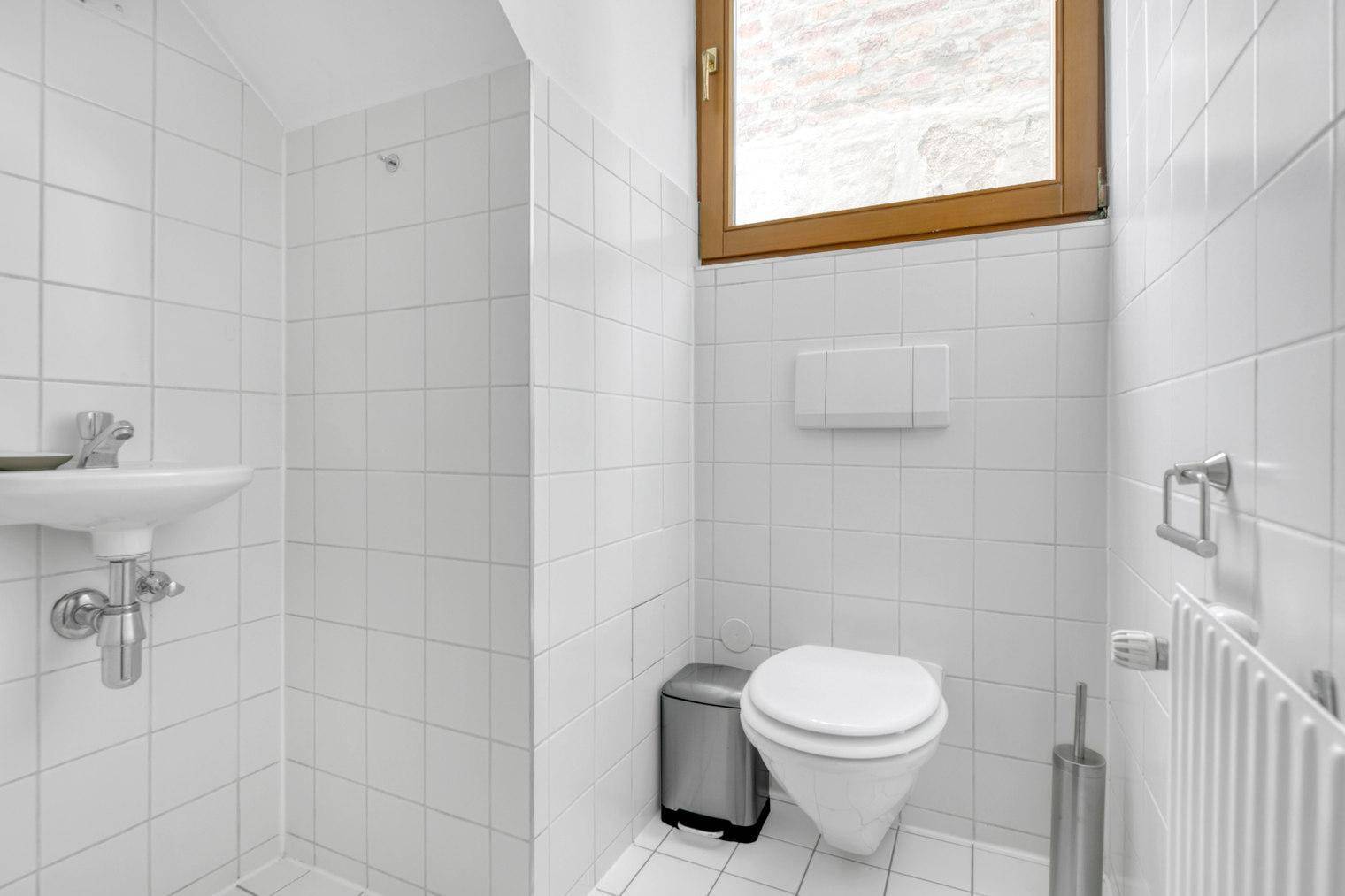 Separate Toilette mit Fenster, Wand-WC und kleinem Handwaschbecken.