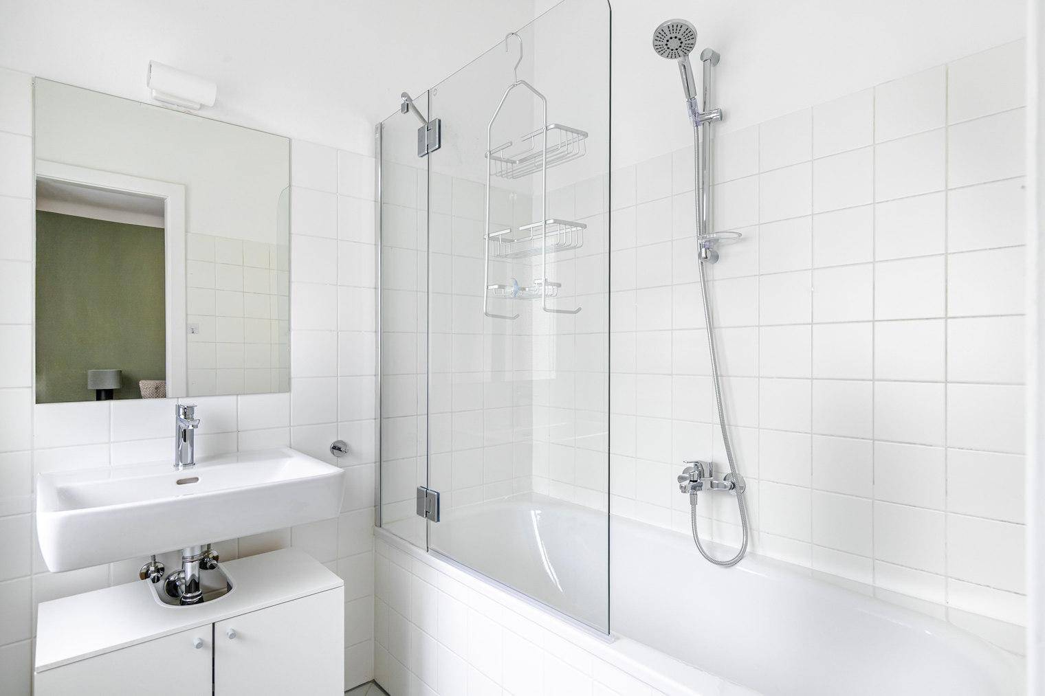 Helles Badezimmer mit Badewanne, Duschabtrennung aus Glas und weißem Waschbecken.