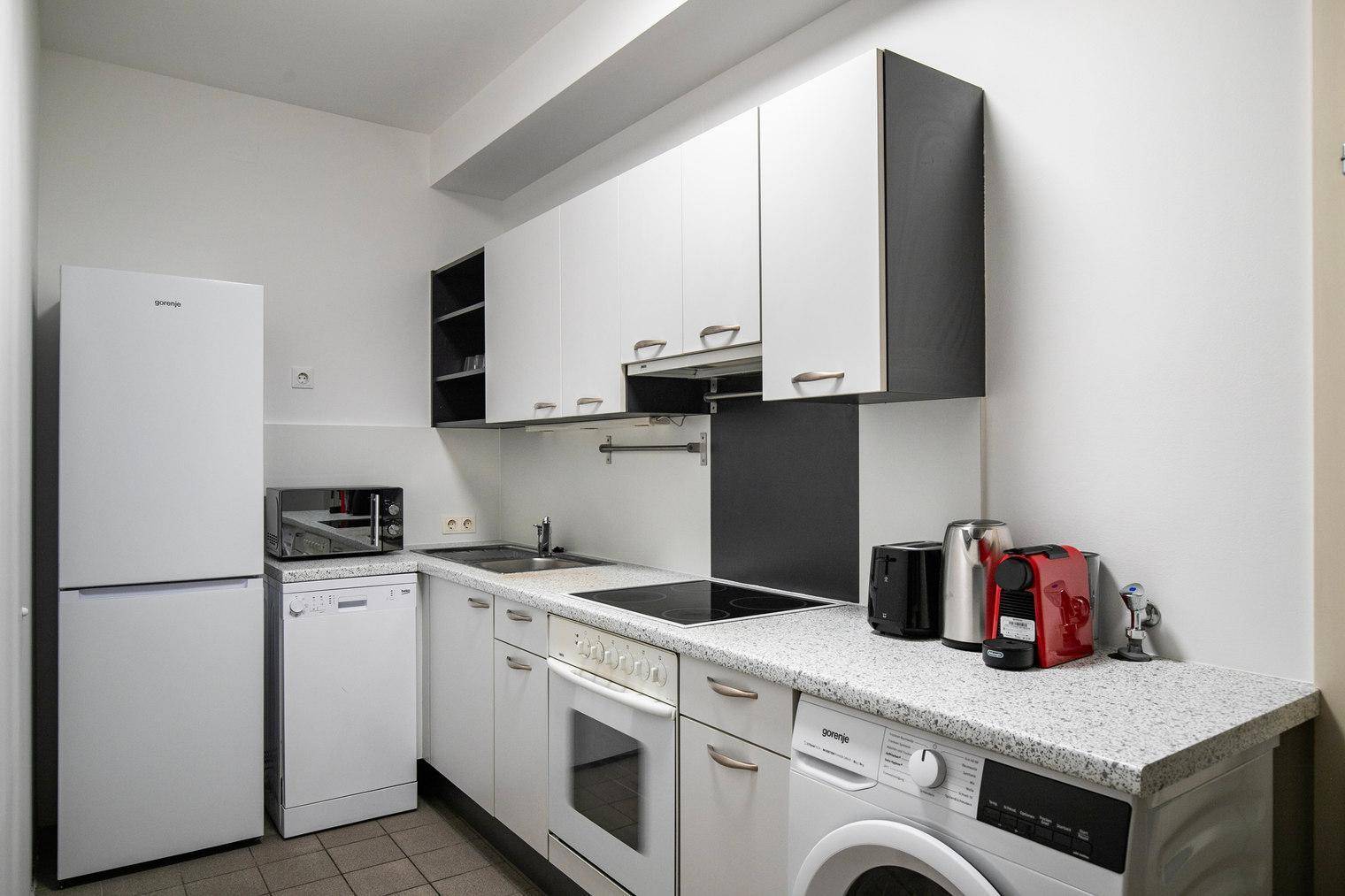 Funktionale Küche mit weißen Schränken, integrierten Geräten und Waschmaschine.