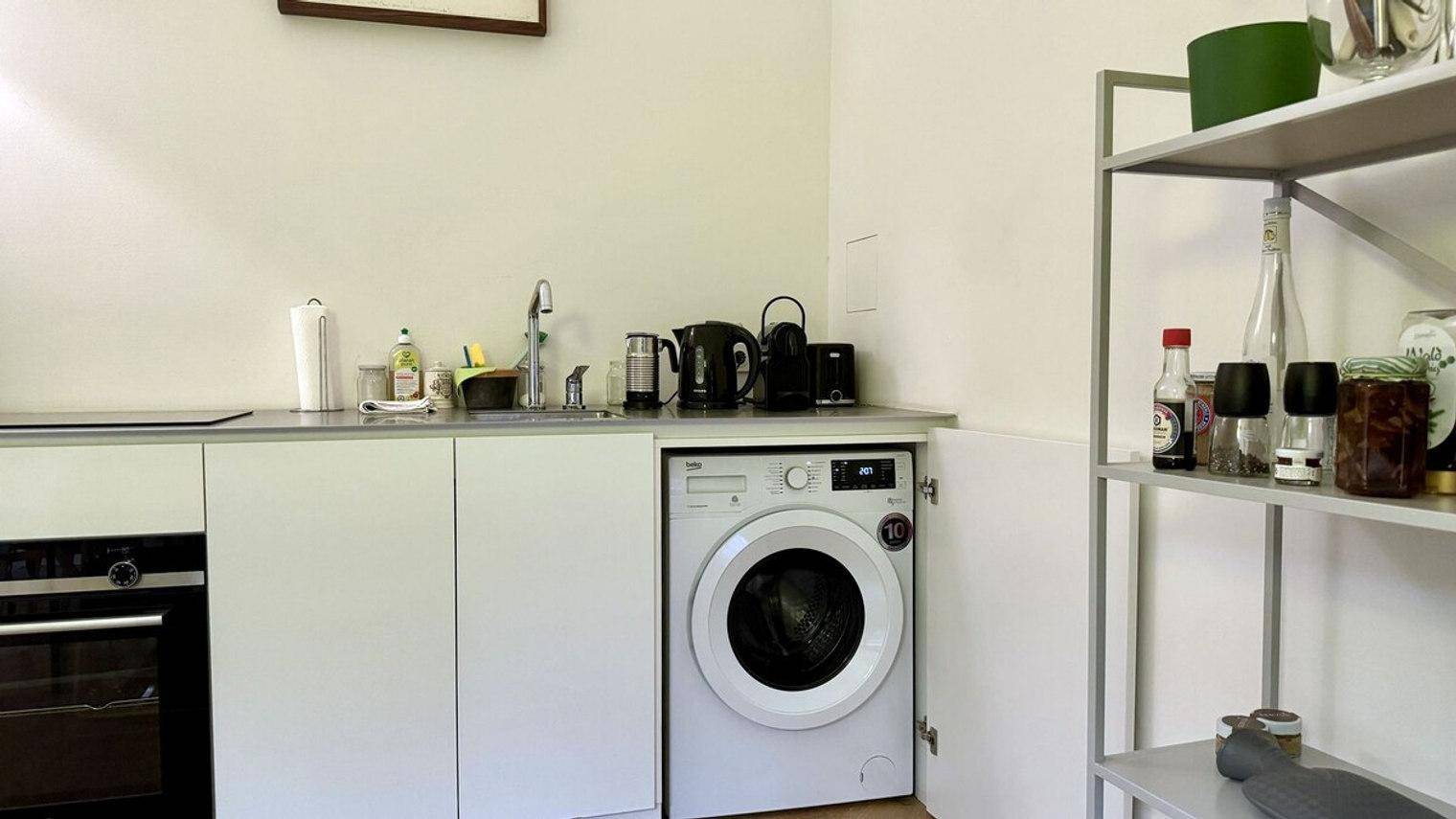 Praktische Küchenzeile mit integrierter Waschmaschine und offenem Regal für Stauraum.
