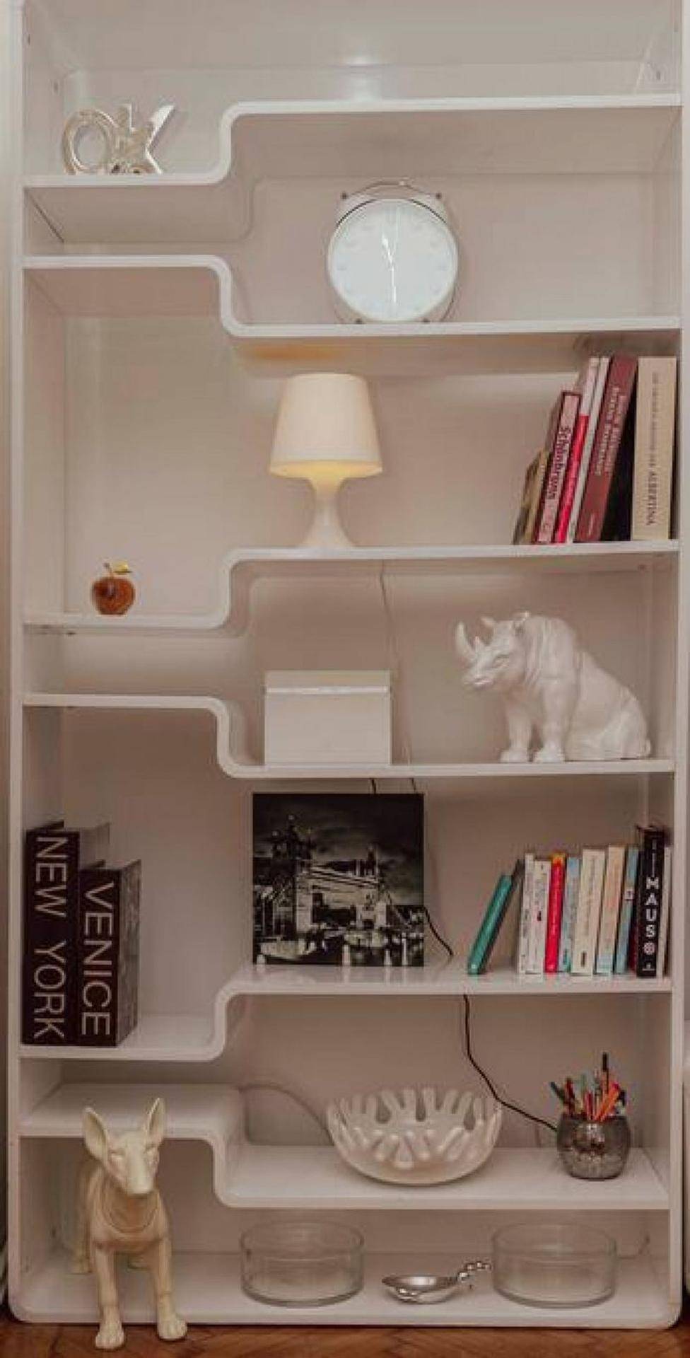 Modernes, weißes Bücherregal mit geschwungenen Regalböden und dekorativen Elementen.