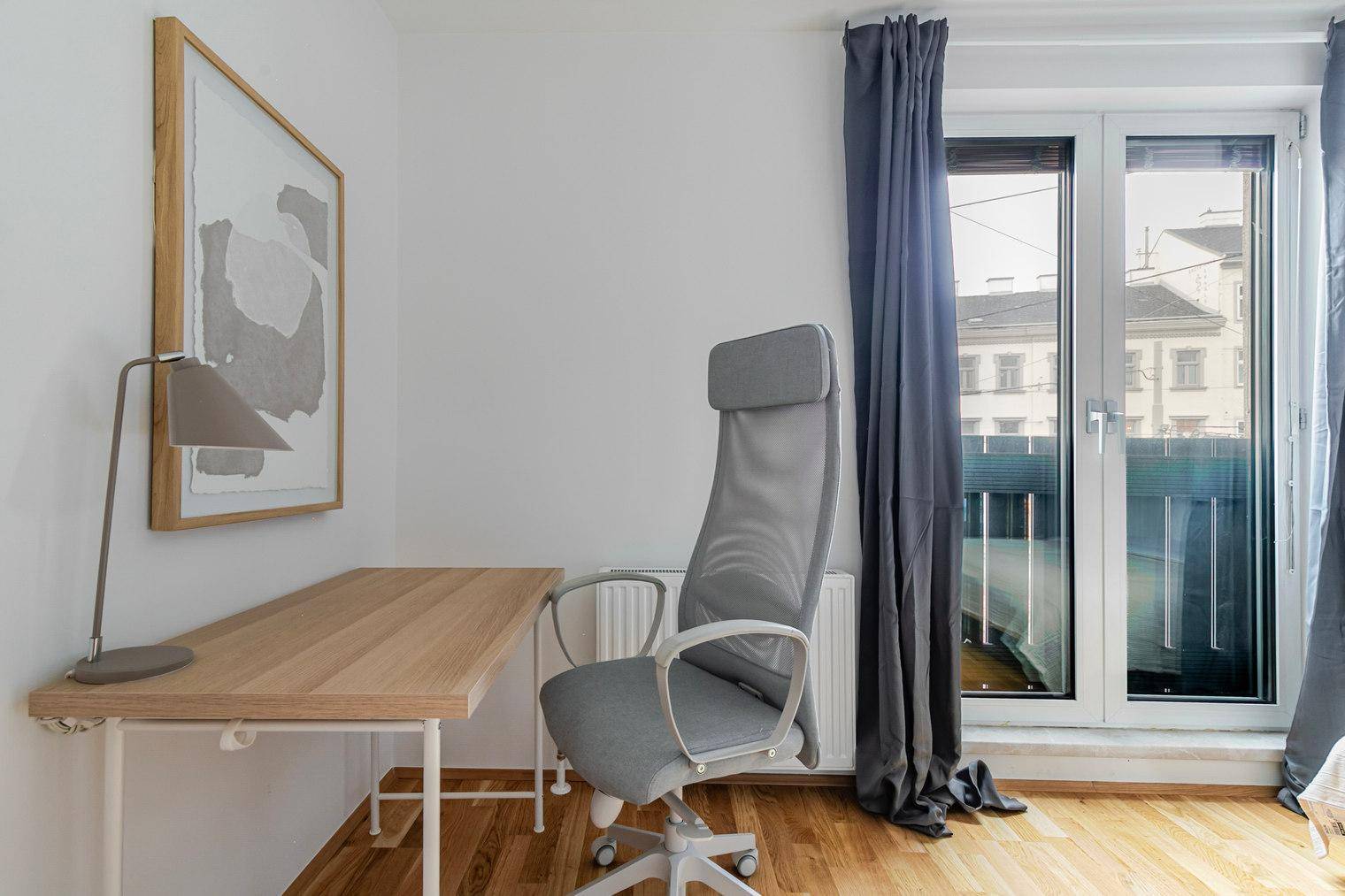 Arbeitsbereich im Schlafzimmer mit Schreibtisch, Bürostuhl und Fenster mit Vorhängen.