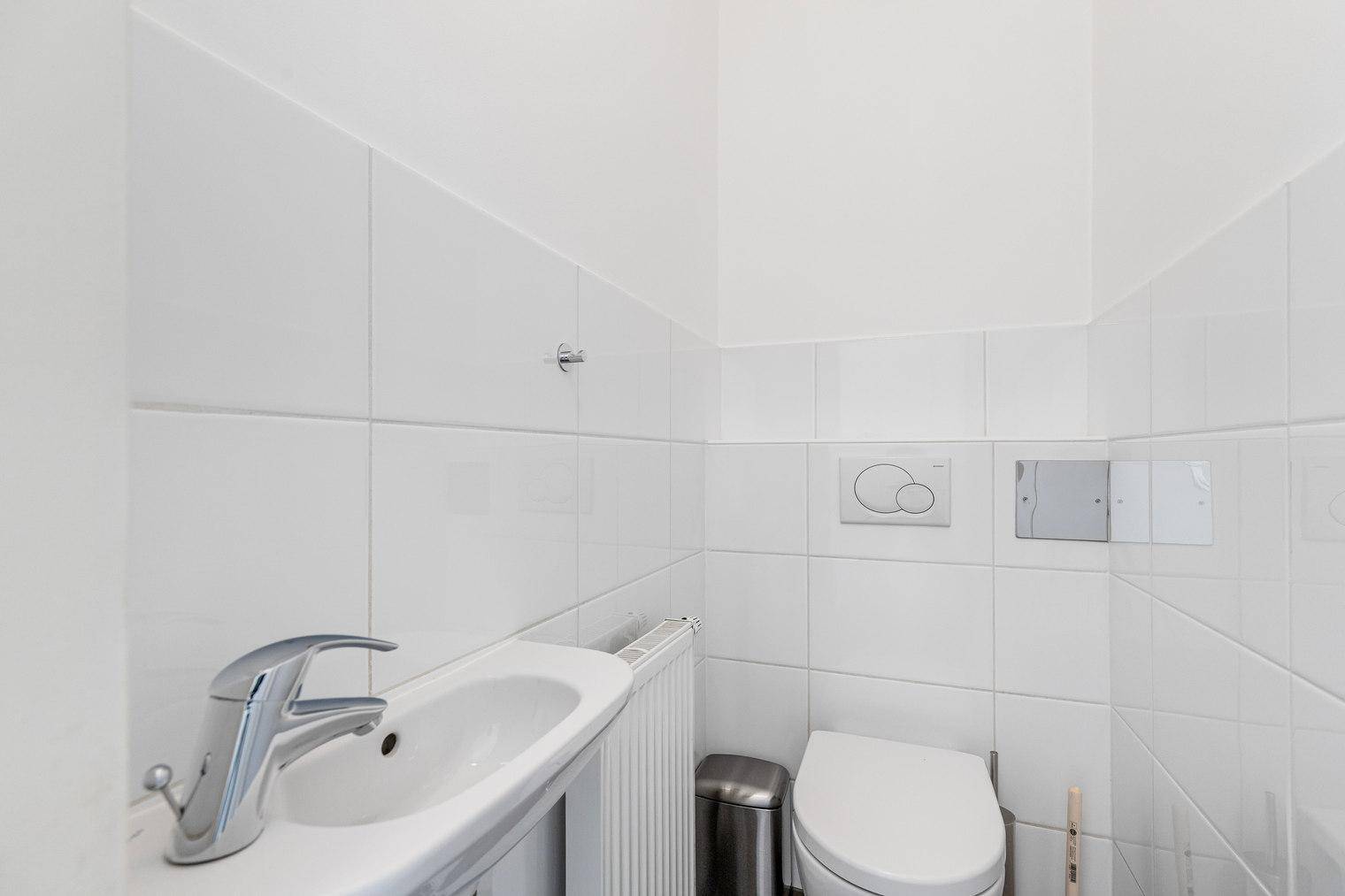 Kleines, hell gefliestes Gäste-WC mit wandmontierter Toilette und Waschbecken.