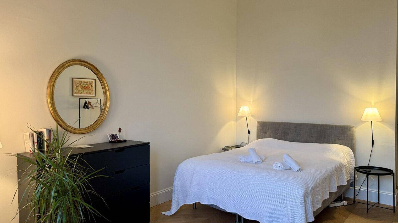 Gemütliches Schlafzimmer mit Doppelbett, Nachttischen und einem großen runden Spiegel.