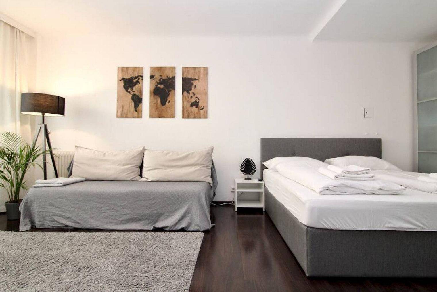 Heller Wohn- und Schlafbereich mit Sofa, Doppelbett und dunklem Holzboden.