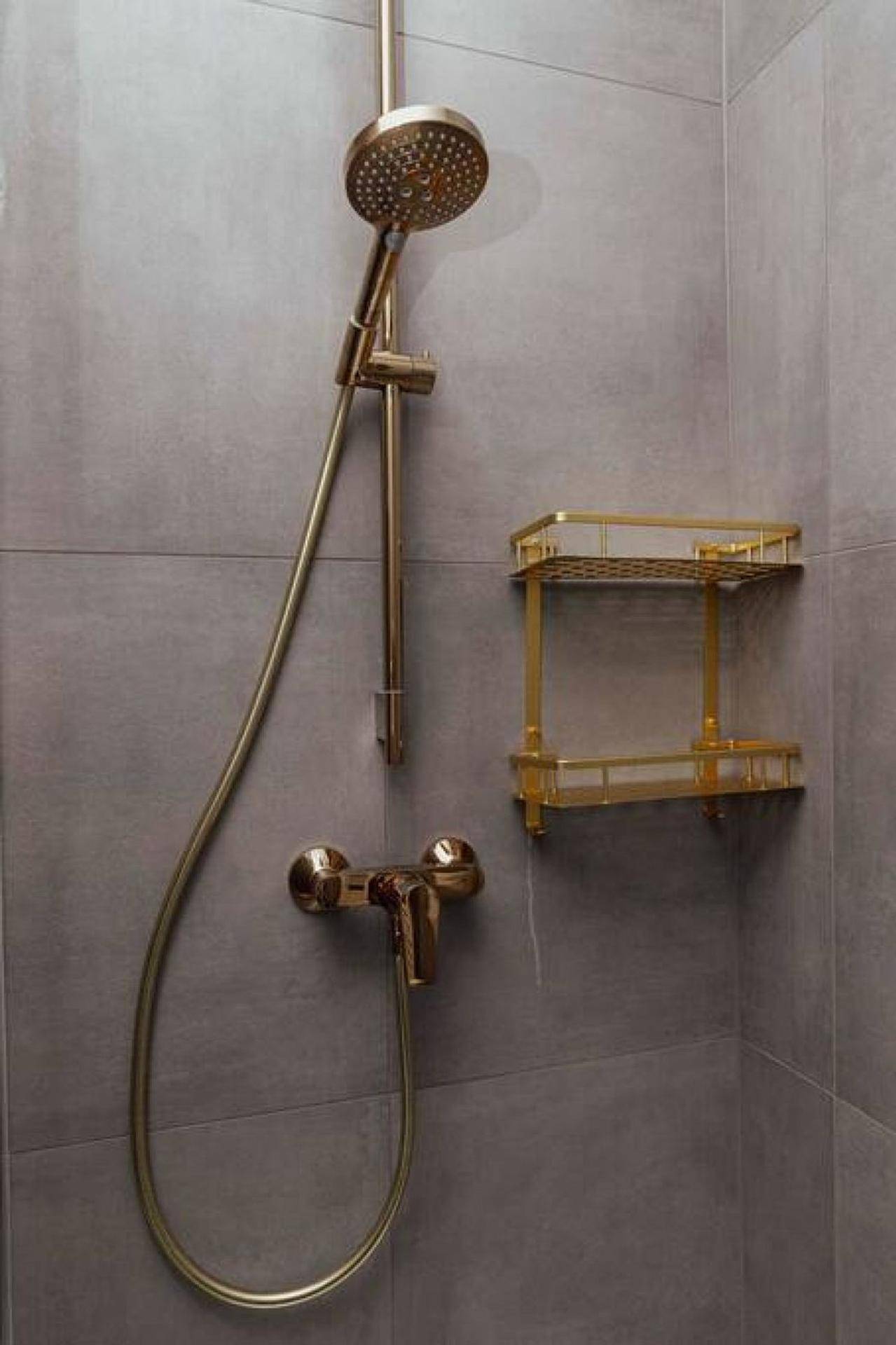 Moderne Dusche mit goldfarbenen Armaturen und Ablage in einem elegant gefliesten Badezimmer.