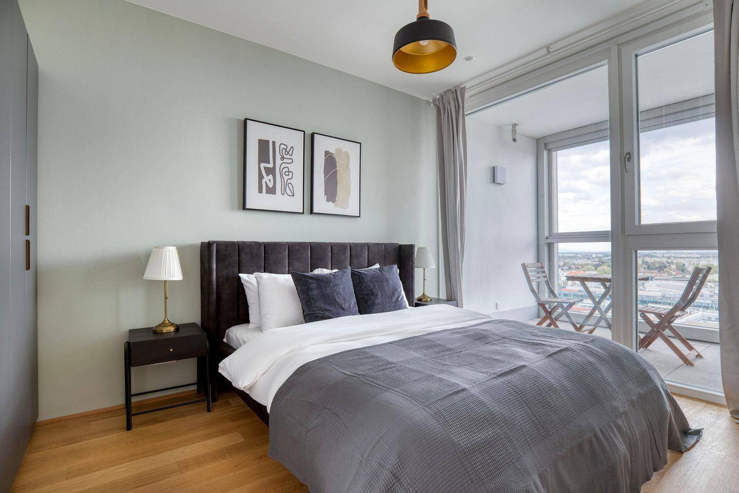 Helles Schlafzimmer mit Doppelbett, Nachttischen und Zugang zu einem Balkon mit Stadtblick.