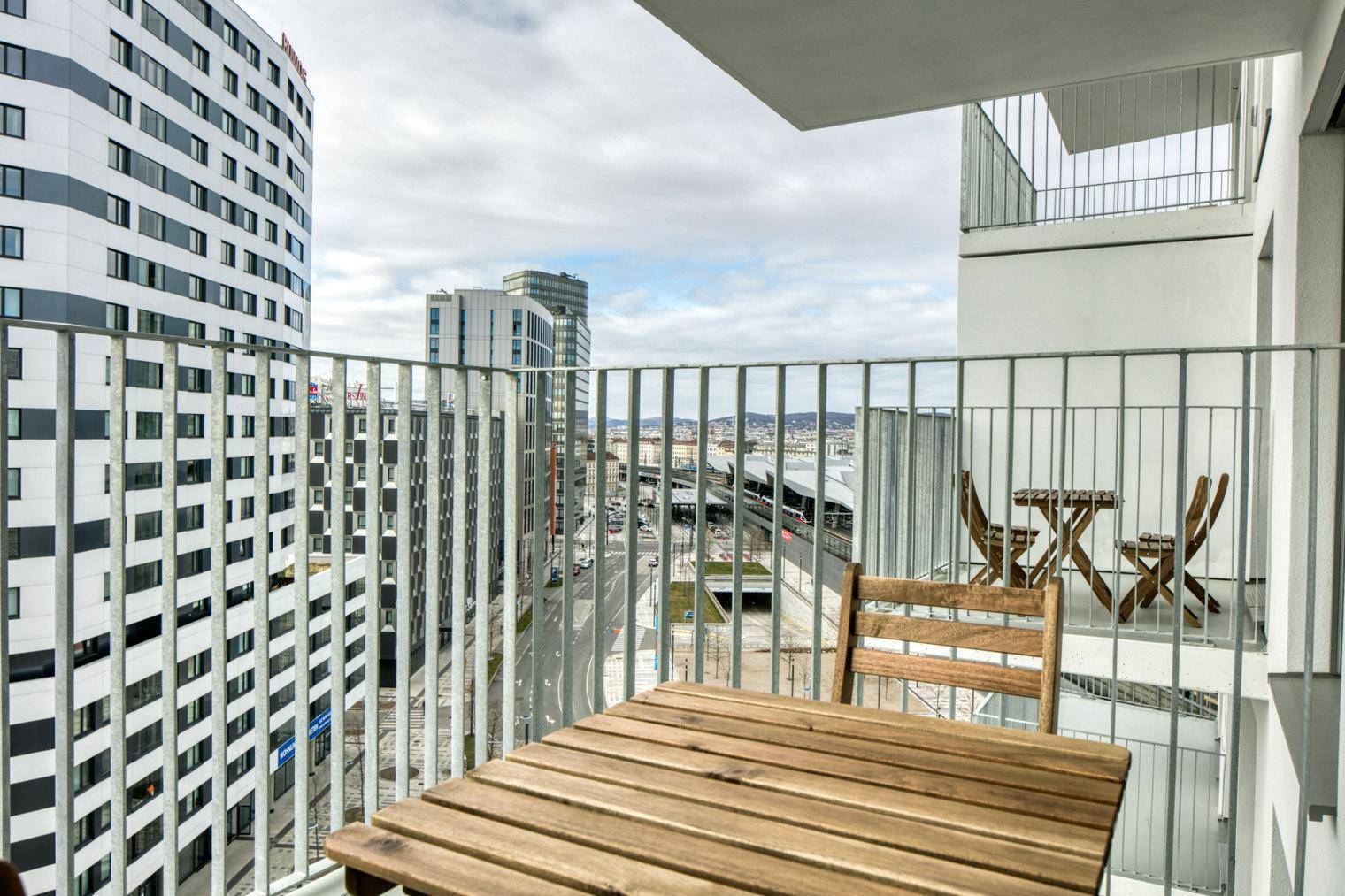 Balkon mit Holztisch und Stühlen bietet einen weiten Blick auf die Stadt und umliegende Gebäude.