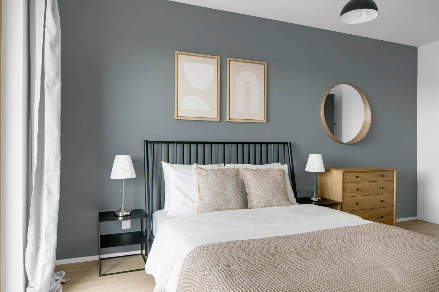 Modernes Schlafzimmer mit Doppelbett, Nachttischen und Kommode vor einer grauen Wand.