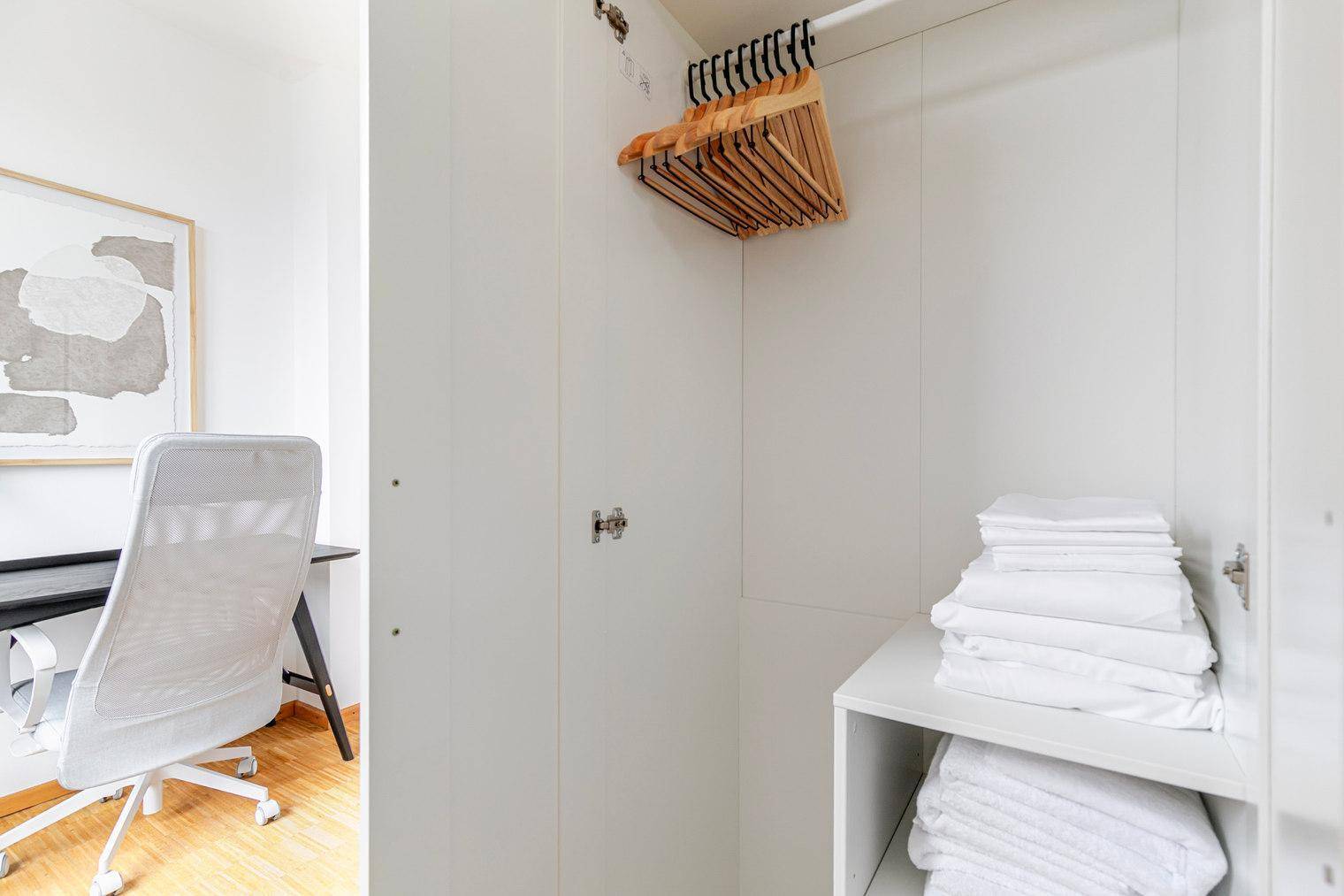 Offener Kleiderschrank mit Kleiderbügeln und gestapelter Wäsche im Arbeitszimmer.