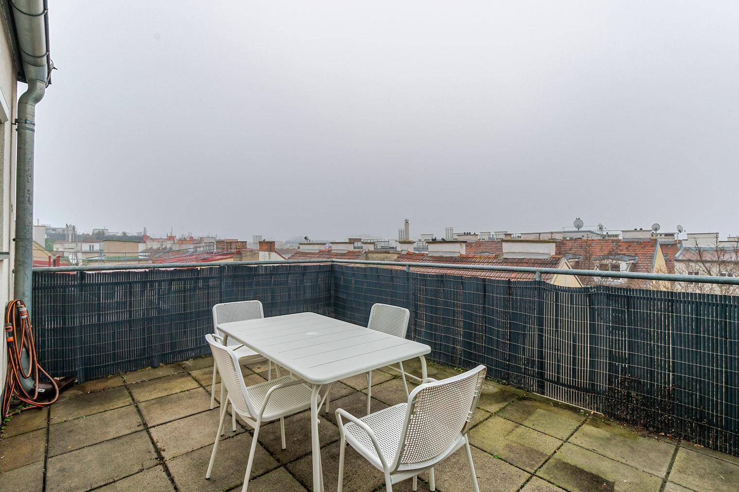 Dachterrasse mit Gartenmöbeln und Blick über die Dächer der Stadt an einem bewölkten Tag.