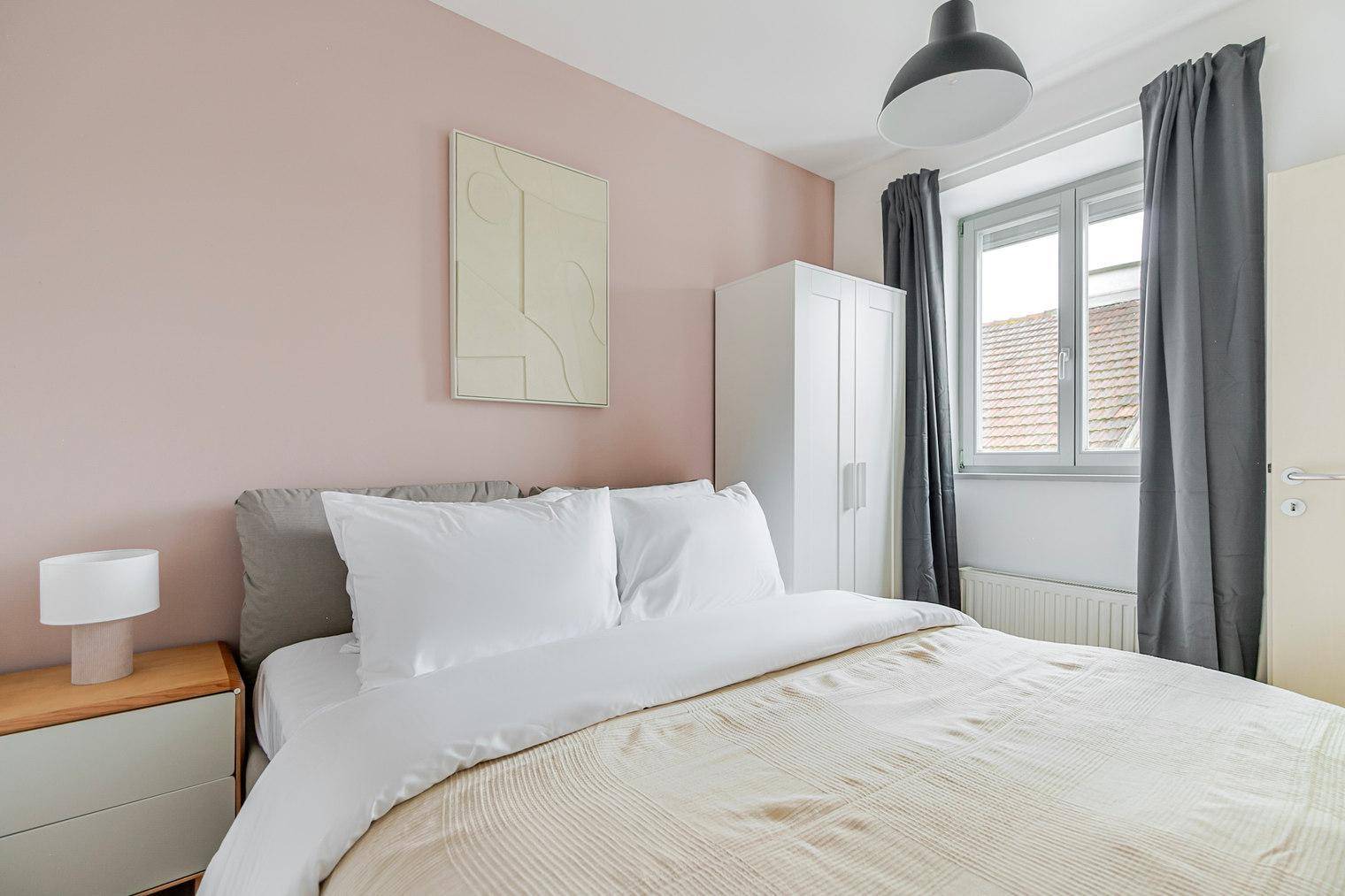 Schlafzimmer mit Doppelbett, Kleiderschrank und Fenster mit dunklen Vorhängen.