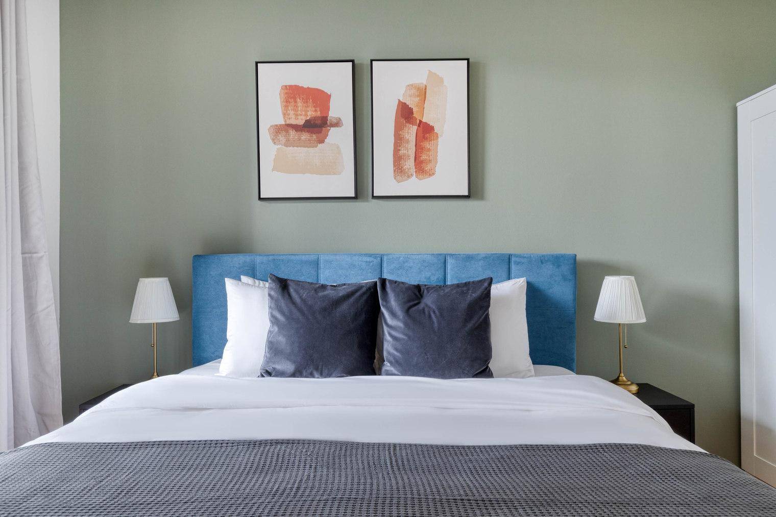 Gemütliches Schlafzimmer mit blauem Bett, Nachttischen und moderner Wandkunst.