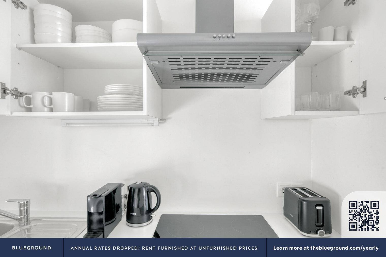 Detailansicht der modernen Küchenzeile mit Kochfeld, Dunstabzugshaube und Geschirr in den Schränken.