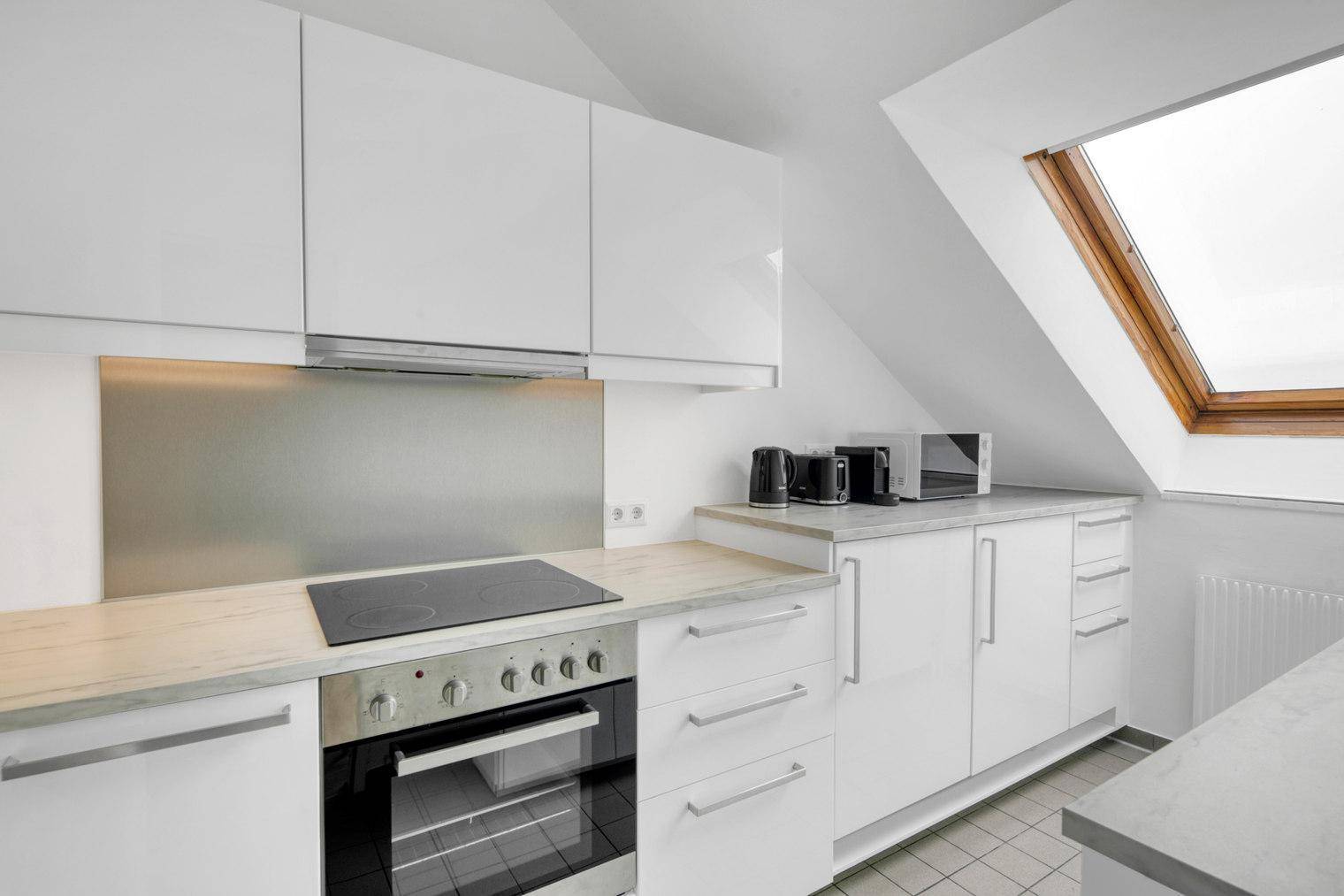 Moderne Küchenzeile mit weißen Schränken, Induktionskochfeld und Dachfenster.