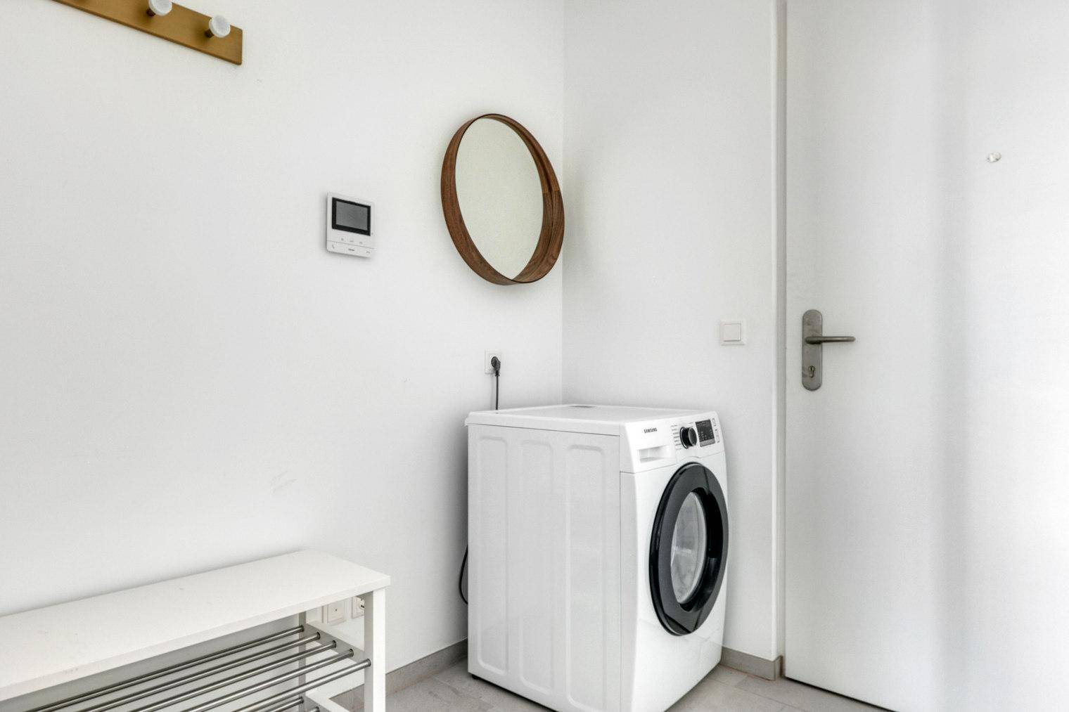 Eingangsbereich mit Waschmaschine, Schuhregal und ovalem Spiegel an der Wand.