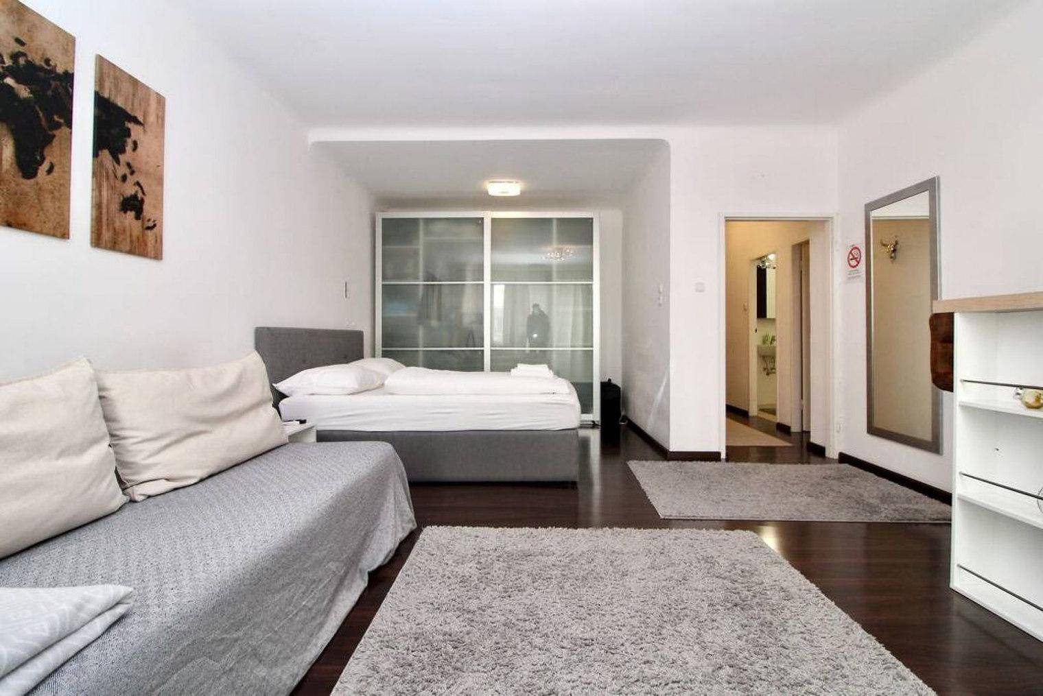 Geräumiges Schlafzimmer mit Doppelbett, Sofa und dunklem Holzboden sowie Schiebetürenschrank.
