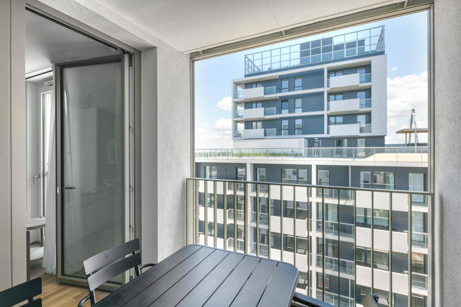 Balkon mit Esstisch und Stühlen, bietet einen weiten Blick auf moderne Gebäude.