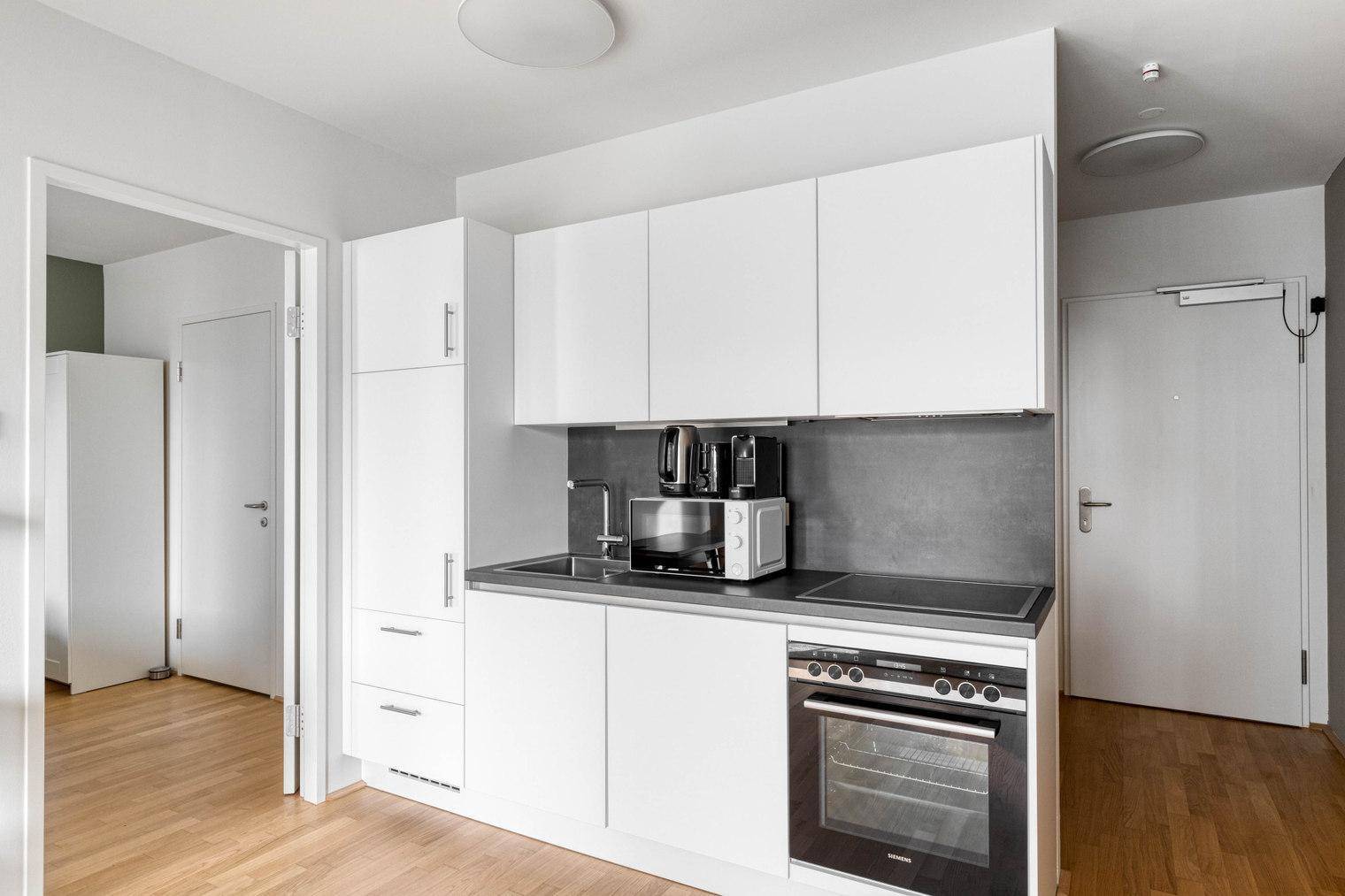 Moderne Küchenzeile mit weißen Schränken, integriertem Backofen und Mikrowelle.