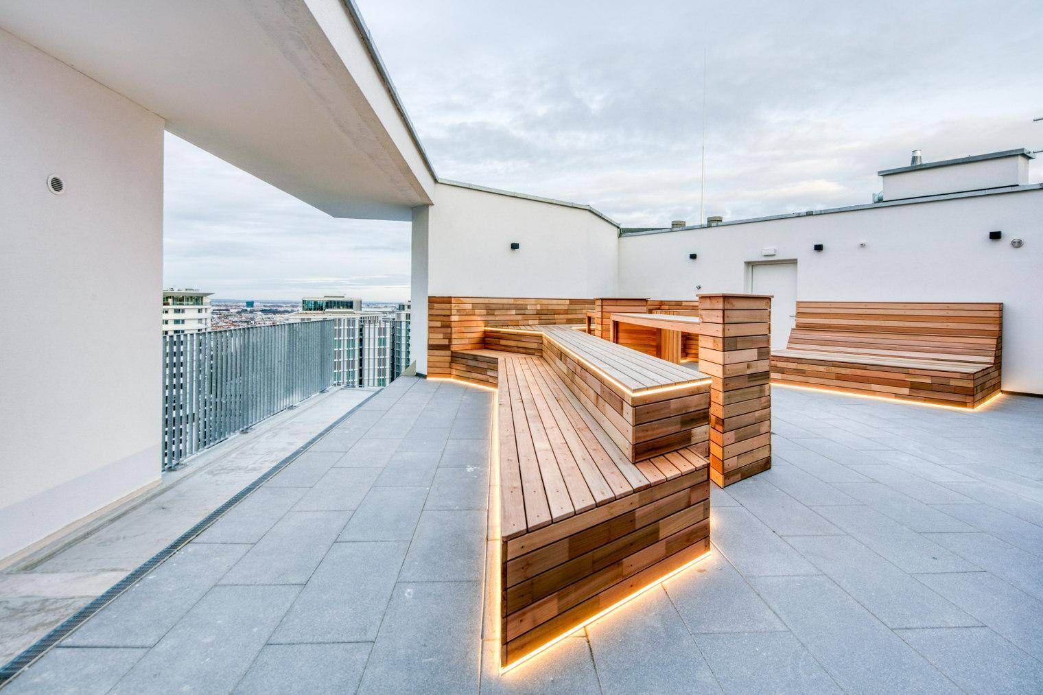 Moderne Dachterrasse mit Holzsitzelementen und integrierter Beleuchtung, bietet Stadtblick.