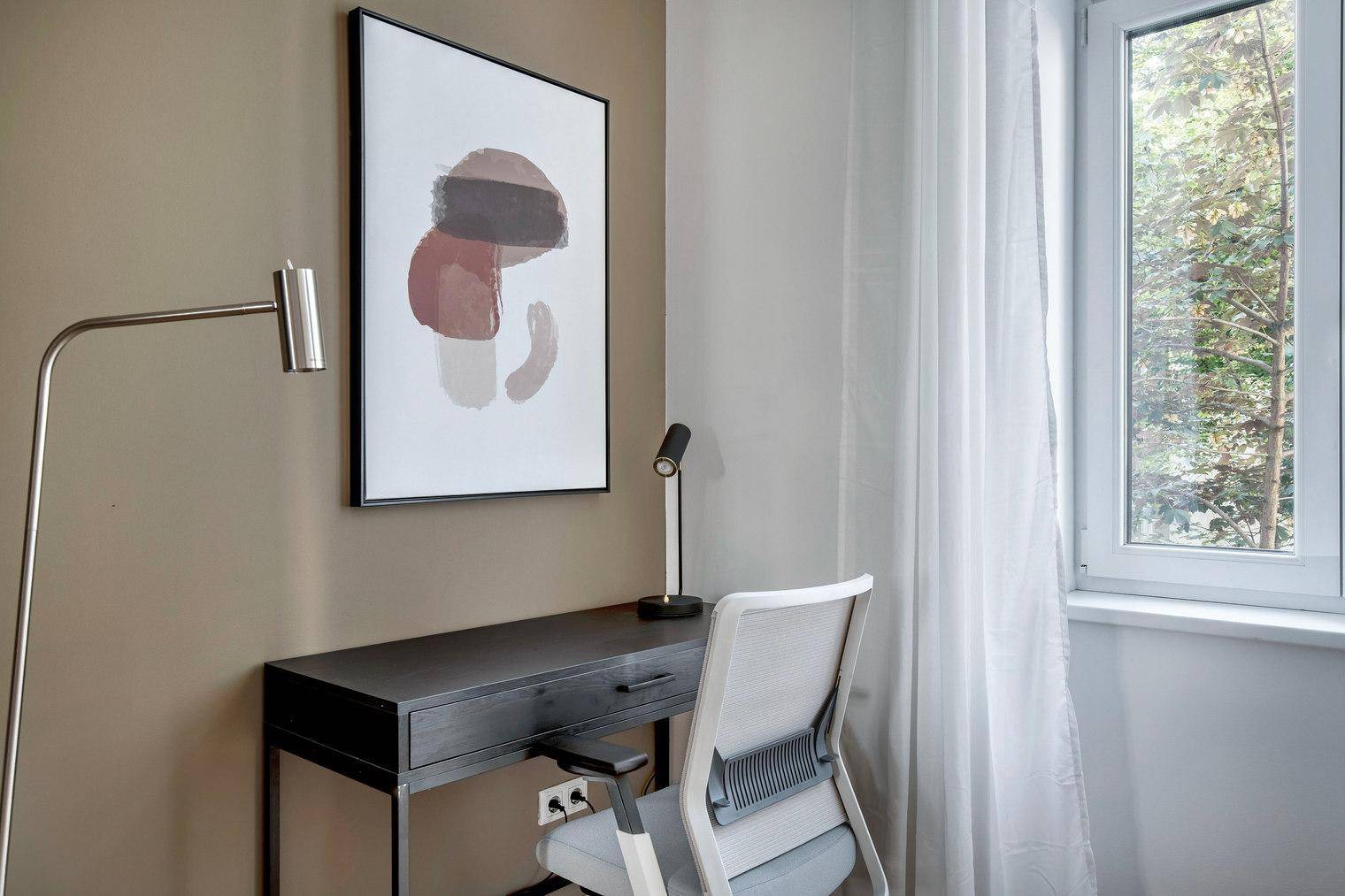 Heller Arbeitsbereich mit Schreibtisch, Bürostuhl und Fensterblick ins Grüne.