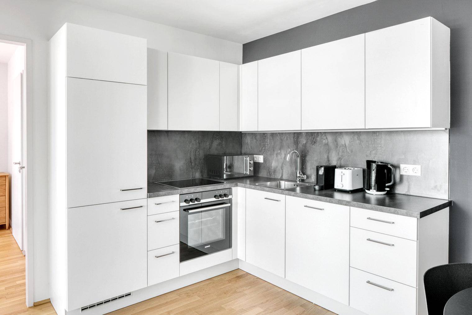 Moderne Einbauküche mit weißen Schränken, integrierten Geräten und Holzboden.
