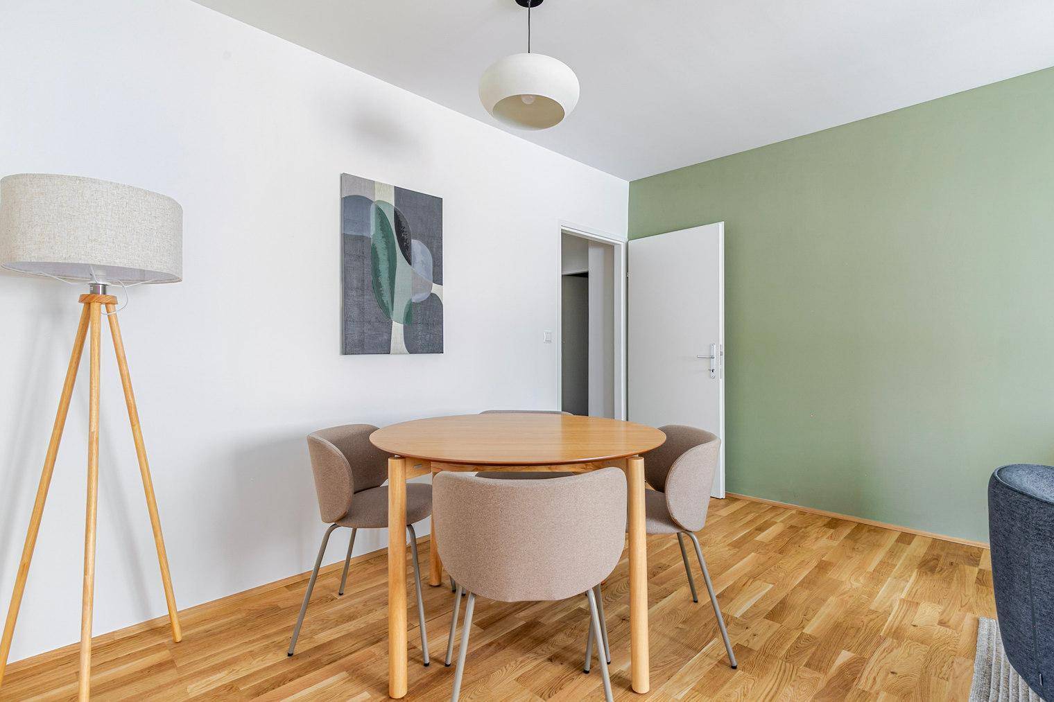 Heller Essbereich mit rundem Holztisch und vier modernen Stühlen, beleuchtet von einer Deckenlampe.