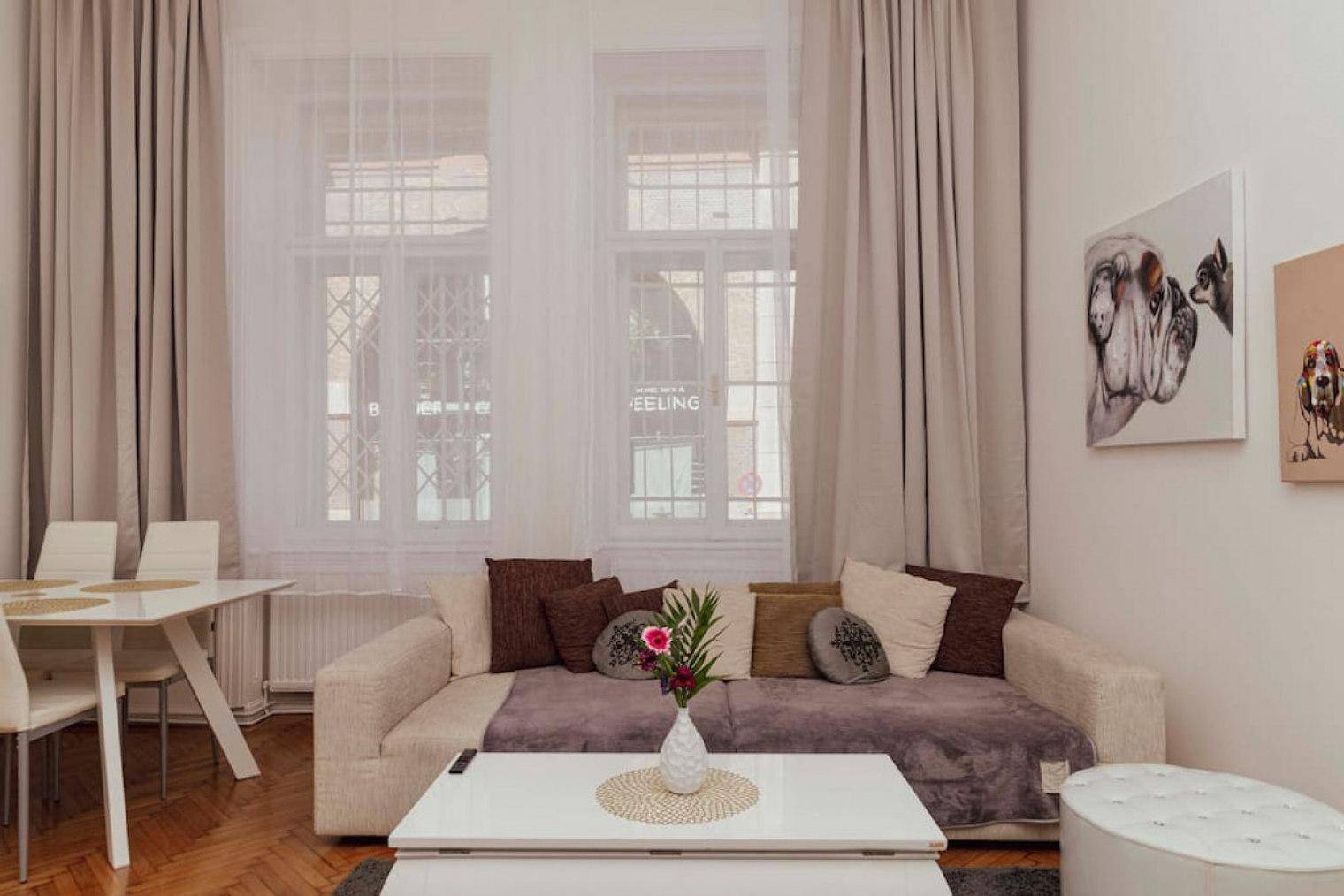 Heller Wohn- und Essbereich mit beigem Sofa, Esstisch und großen Fenstern mit Vorhängen.
