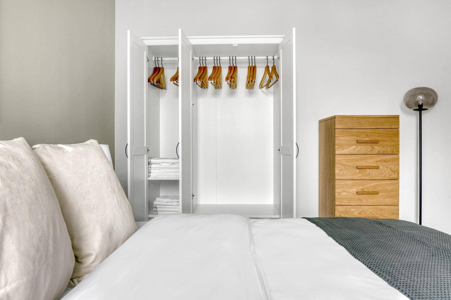 Schlafzimmer mit offenem Kleiderschrank, Holzbett und Kommode.