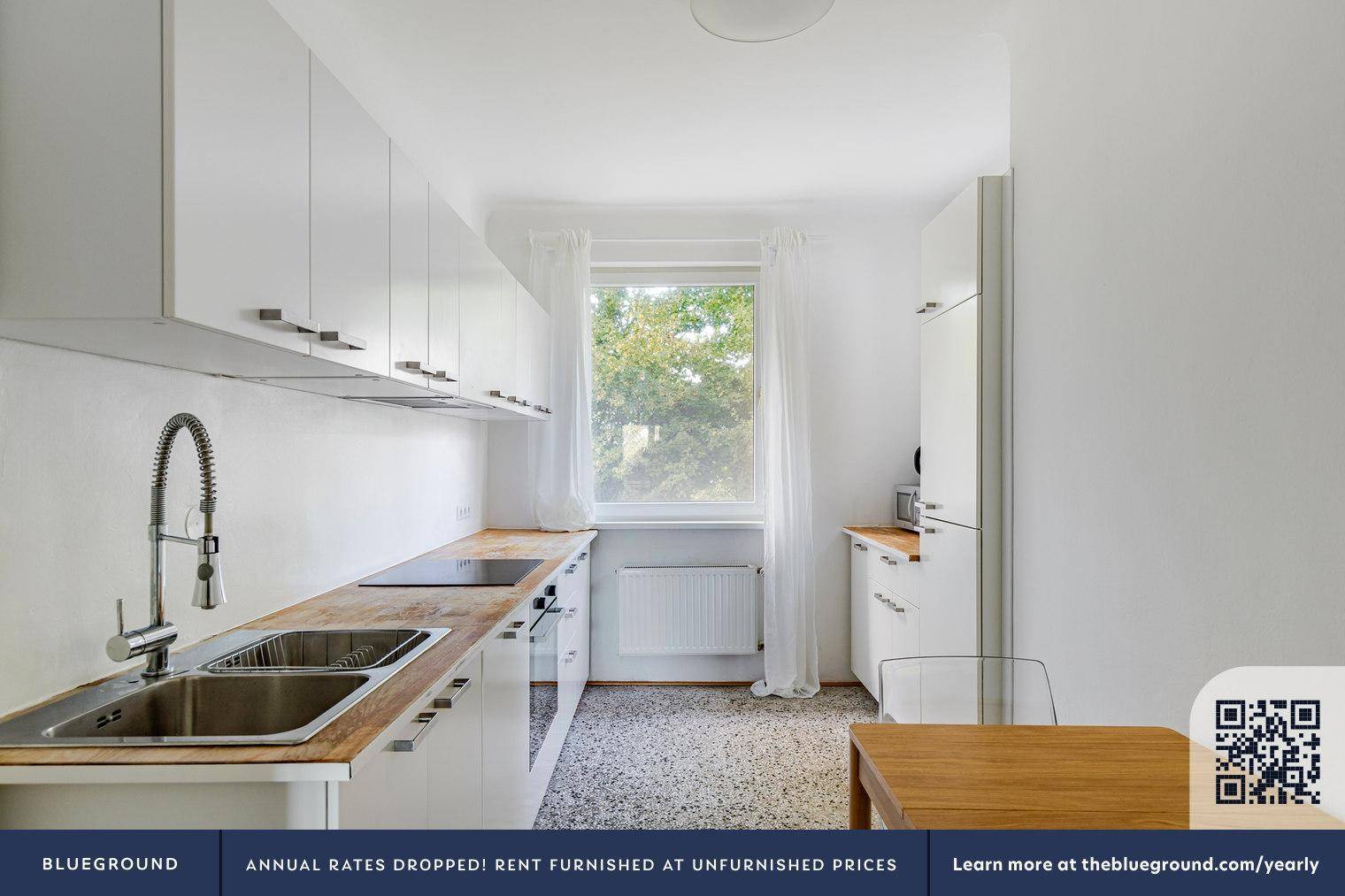 Helle Küche mit weißen Schränken, Holz-Arbeitsplatten und Fenster mit Blick ins Grüne.