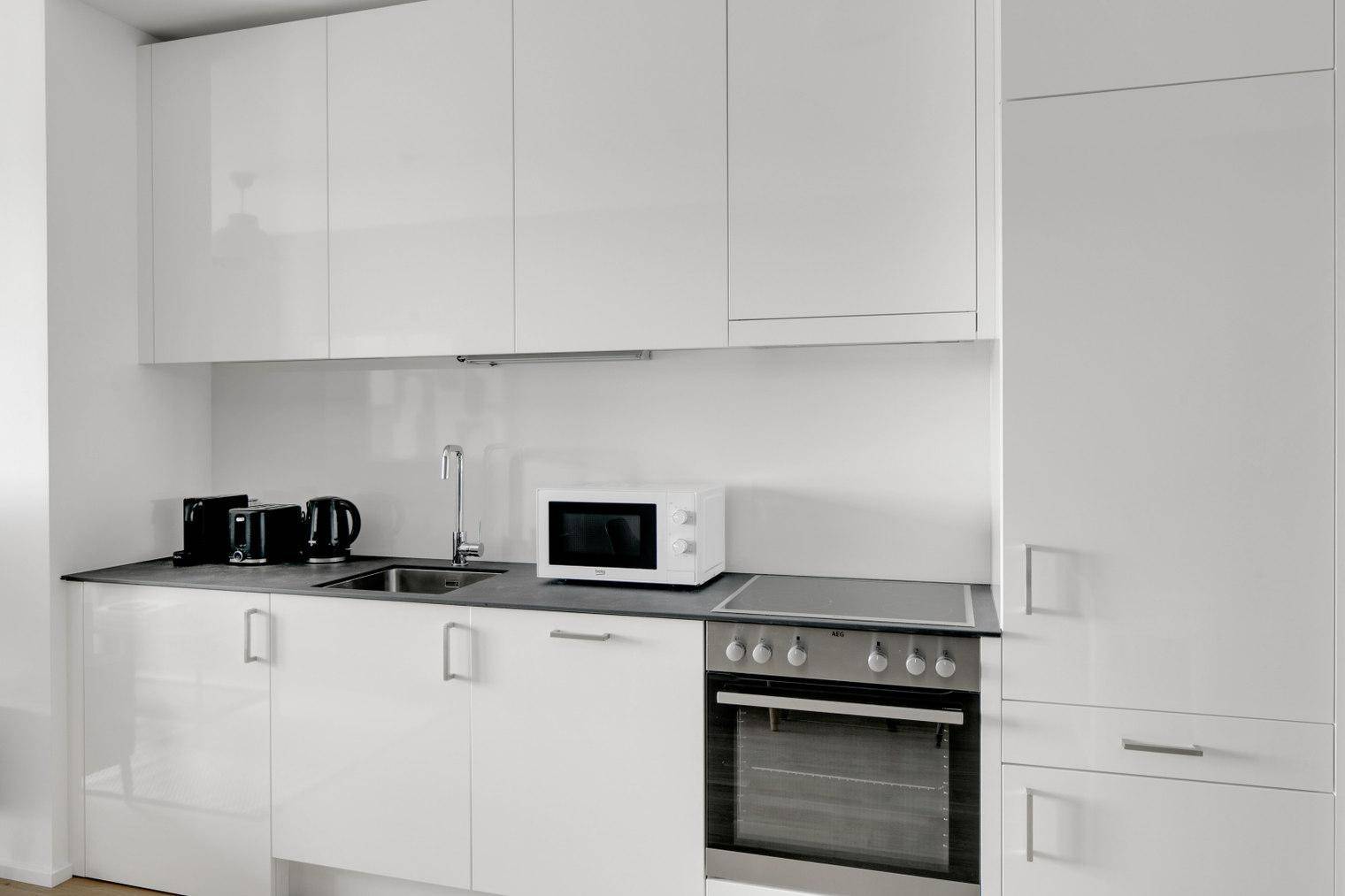 Moderne Küchenzeile mit weißen Hochglanzschränken, integriertem Backofen und Mikrowelle.