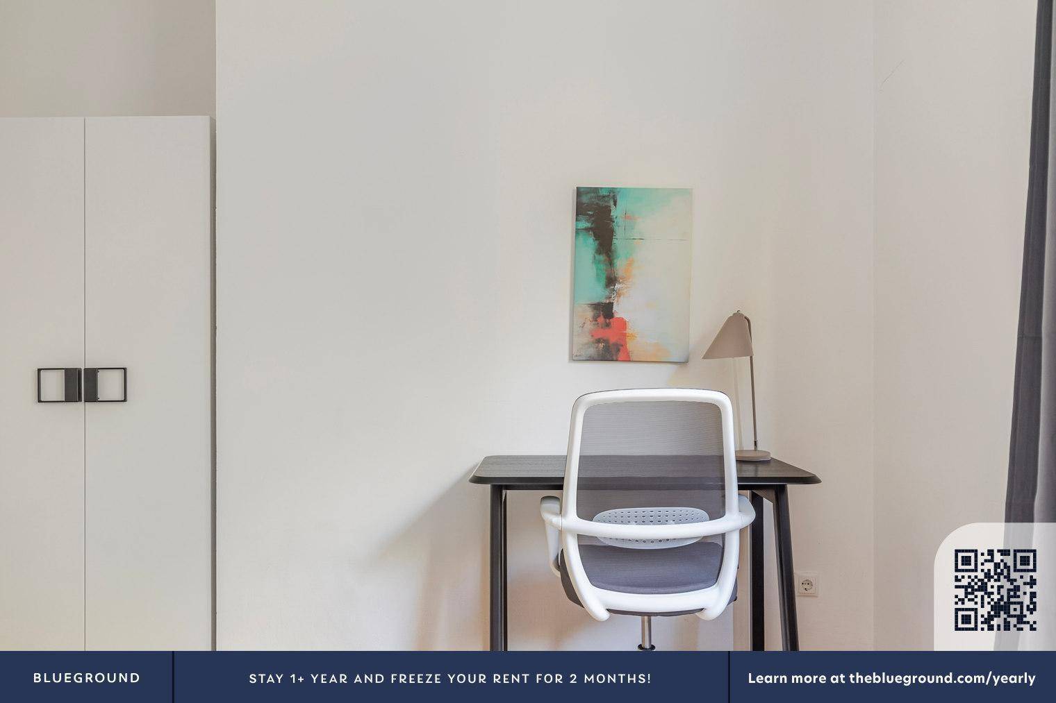 Schreibtisch mit Bürostuhl und Kunstwerk an der Wand in einem hellen Schlafzimmer.