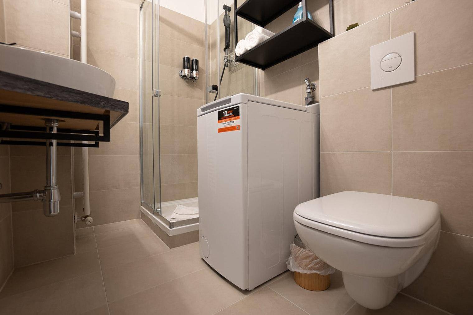 Modernes Badezimmer mit Waschbecken, Dusche, Waschmaschine und WC, komplett ausgestattet.