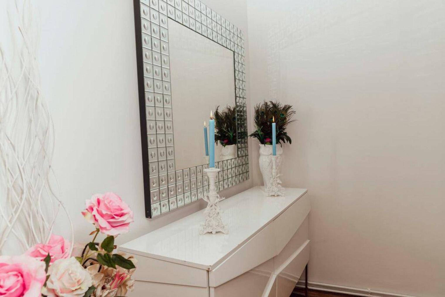 Kommode mit dekorativem Spiegel, Blumen und Kerzen im Schlafzimmer.